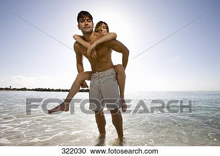 Man giving woman a piggyback on beach View Large Photo Image Stock Image - Man giving woman a piggyback on beach. Fotosearch