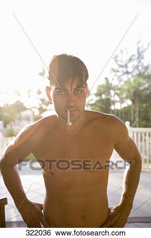 Stock Photograph - Man standing bare cheated with hands on hips and smoking a cigarette. Fotosearch