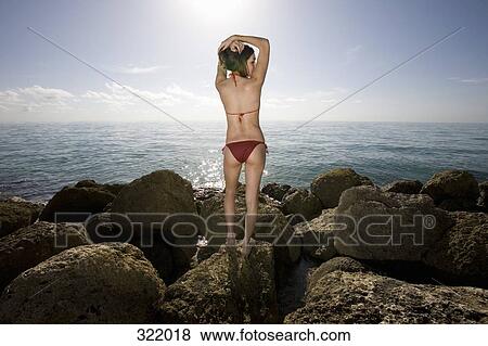 Rear view of woman standing on rock in front of sea View Large Photo Image Stock Photo - Rear view of woman standing on rock in front of sea. Fotosearch