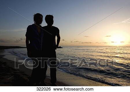Stock Photograph - Young couple embracing on beach at sunset. Fotosearch