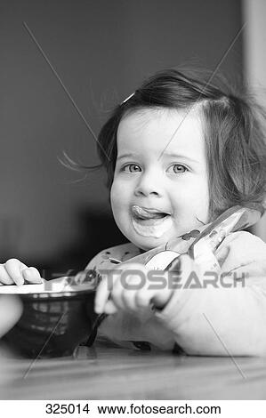 Picture - Girl eating food at table. Fotosearch