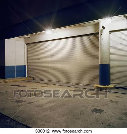 Stock Image - Floodlights above rolling garage doors at loading dock. Fotosearch