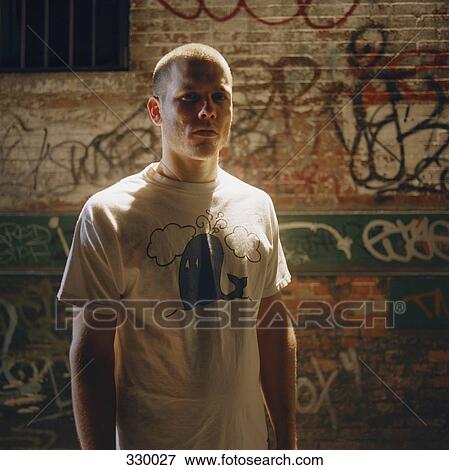 Young man standing in front of brick wall covered in graffiti View Large Photo Image Stock Photo - Young man standing in front of brick wall covered in graffiti. Fotosearch
