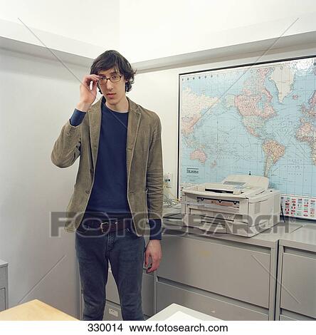 Young man standing in office View Large Photo Image Picture - Young man standing in office. Fotosearch