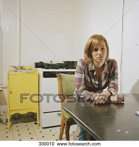 Young woman sitting at table in kitchen View Large Photo Image Stock Image - Young woman sitting at table in kitchen. Fotosearch