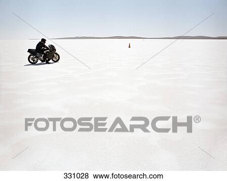 Man sitting on motorcycle on salt flat View Large Photo Image Stock Photo - Man sitting on motorcycle on salt flat. Fotosearch