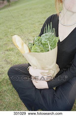 Woman sitting in a park and holding a bag of groceries View Large Photo Image Stock Photo - Woman sitting in a park and holding a bag of groceries. Fotosearch