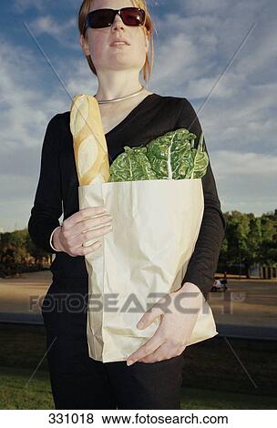 Woman standing in a park and holding a bag of groceries View Large Photo Image Stock Photo - Woman standing in a park and holding a bag of groceries. Fotosearch
