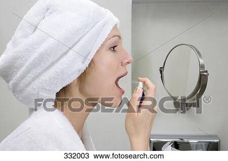 Stock Image - Woman spraying breath freshener in bathroom. Fotosearch