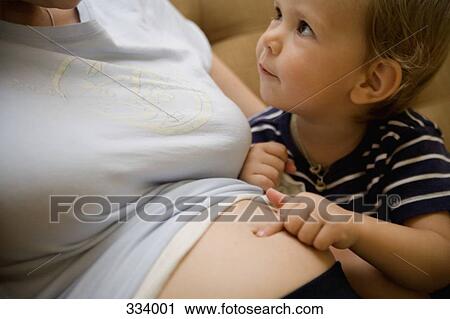 Stock Image - Child pointing to pregnant mother’s abdomen. Fotosearch
