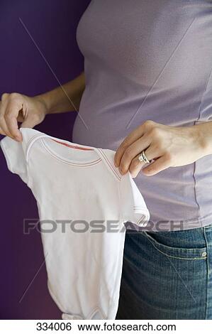 Pregnant woman holding baby clothing View Large Photo Image Stock Photograph - Pregnant woman holding baby clothing. Fotosearch