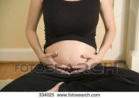 Stock Photography - Pregnant woman sitting and holding abdomen. Fotosearch