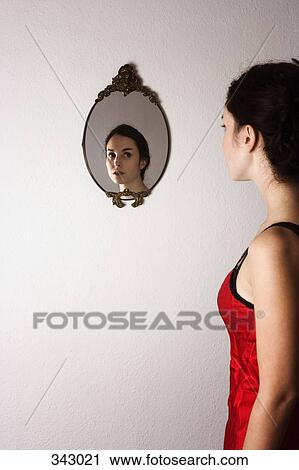 Stock Image - Reflection of young woman in ornate mirror on wall. Fotosearch