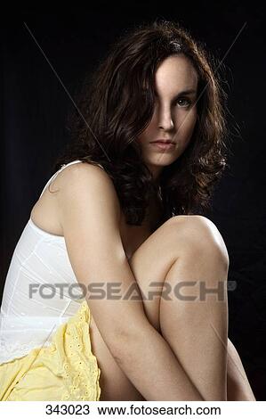 Stock Image - Young woman sitting with leg curled up. Fotosearch