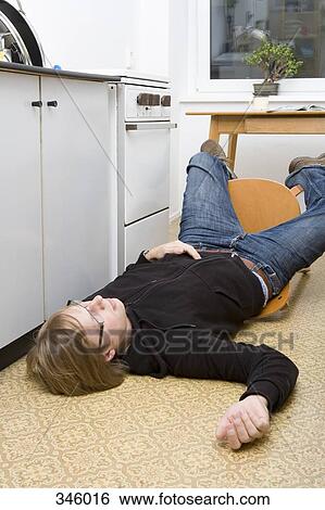 Young man lying on the ground after falling back in a chair View Large Photo Image Stock Photograph - Young man lying on the ground after falling back in a chair. Fotosearch