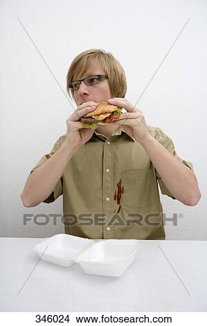 Young man spilling ketchup on his shirt whilst eating a hamburger View Large Photo Image Picture - Young man spilling ketchup on his shirt whilst eating a hamburger. Fotosearch