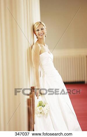 Stock Photo - Bride holding wedding bouquet and leaning against a column. Fotosearch
