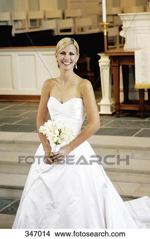 Picture - Bride holding wedding bouquet whilst standing at altar. Fotosearch