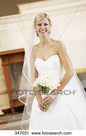 Stock Image - Bride holding wedding bouquet whilst standing at altar. Fotosearch
