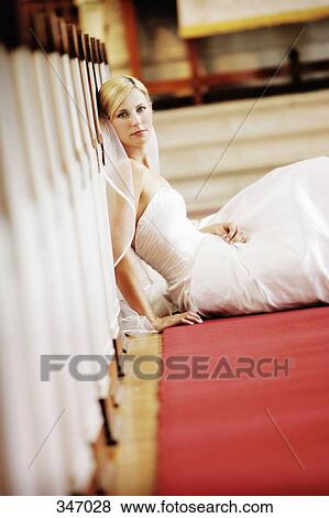 Stock Photo - Bride sitting against pew in church aisle. Fotosearch