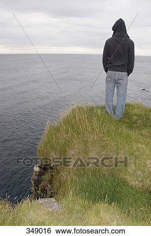 Stock Photograph - Person standing on edge of cliff, looking at horizon. Fotosearch