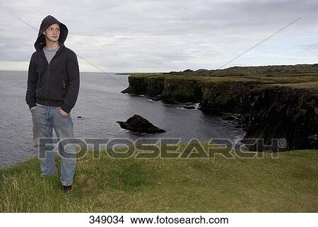 Young man standing at edge of cliff View Large Photo Image Picture - Young man standing at edge of cliff. Fotosearch
