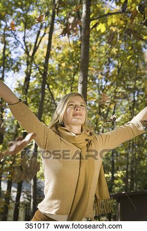 Stock Photo - Woman raising her arms and leaves falling from trees. Fotosearch
