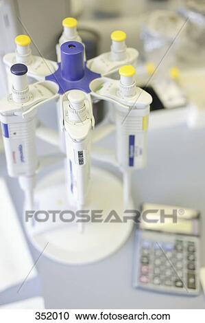 Stock Image - Rack of pipettes and calculator on bench in laboratory. Fotosearch