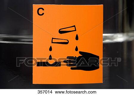 Picture - ‘Corrosive’ label on glass flask containing liquid. Fotosearch