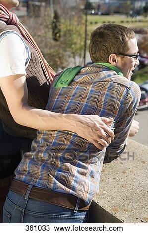 Stock Image - Gay couple leaning against a wall and looking at view. Fotosearch