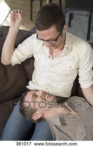 Stock Photo - Gay couple relaxing on the sofa and laughing. Fotosearch