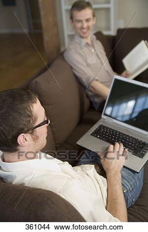 Gay couple using laptop and reading on sofa View Large Photo Image Picture - Gay couple using laptop and reading on sofa. Fotosearch