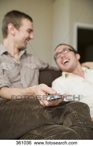 Homosexual couple laughing on sofa together with remote control View Large Photo Image Stock Photograph - Homosexual couple laughing on sofa together with remote control. Fotosearch