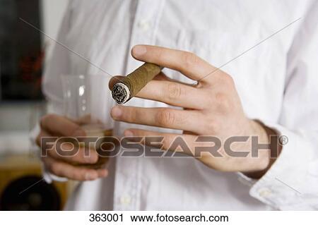 Man holding a glass of whiskey and a cigar View Large Photo Image Stock Image - Man holding a glass of whiskey and a cigar. Fotosearch