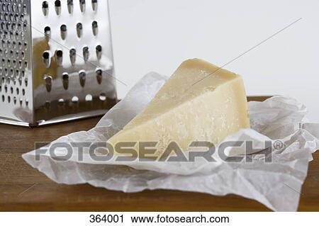 Stock Image - Parmesan cheese and grater on wooden cutting board. Fotosearch