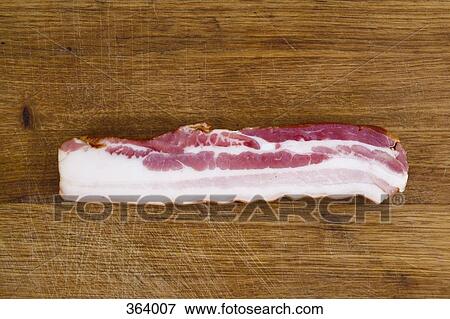 Stock Photo - Slice of bacon on wooden cutting board. Fotosearch