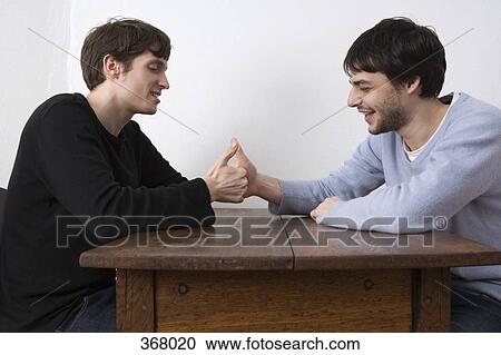 Stock Image - Two young men playing game and laughing at table. Fotosearch