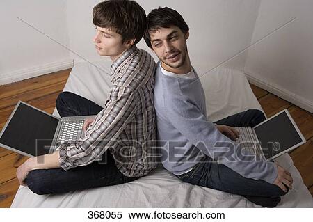 Stock Photography - Two young men sitting back to back using laptops. Fotosearch