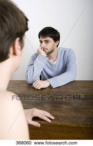 Stock Image - Two young men sitting opposite each other at table. Fotosearch