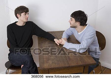 Stock Photograph - Young gay couple holding hands across table. Fotosearch
