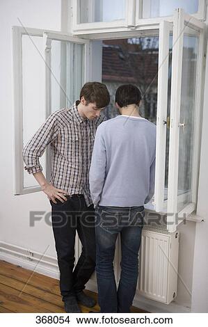 Picture - Young gay couple talking in front of window. Fotosearch