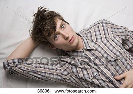 Young man lying on bed and looking at camera View Large Photo Image Stock Image - Young man lying on bed and looking at camera. Fotosearch