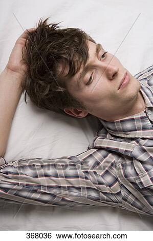 Young man lying on bed thinking View Large Photo Image Stock Photograph - Young man lying on bed thinking. Fotosearch