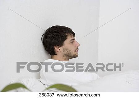 Young man sitting in bed and looking away View Large Photo Image Stock Photo - Young man sitting in bed and looking away. Fotosearch