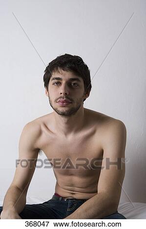 Stock Photo - Young man sitting shirtless on bed. Fotosearch