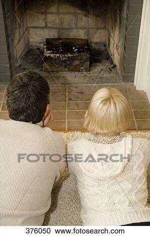 Stock Image - Young couple lying down in front of an open fire together. Fotosearch