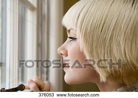 Stock Image - Young woman looking out a window. Fotosearch