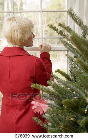 Young woman standing near Christmas tree and looking out a window View Large Photo Image Stock Photo - Young woman standing near Christmas tree and looking out a window. Fotosearch