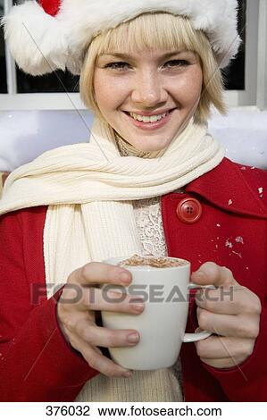 Stock Image - Young woman wearing a Santa hat and holding a mug of hot chocolate. Fotosearch