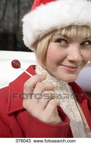 Stock Image - Young woman wearing a Santa hat and holding a lollipop. Fotosearch
